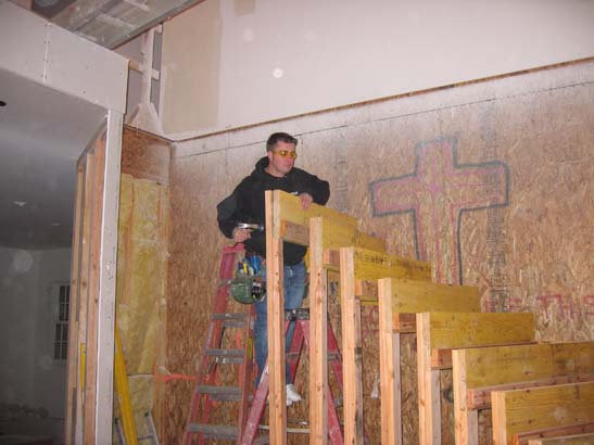 Before photo of a worker standing on a ladder next to a frame of stairs, with a graffitid wall behind him.